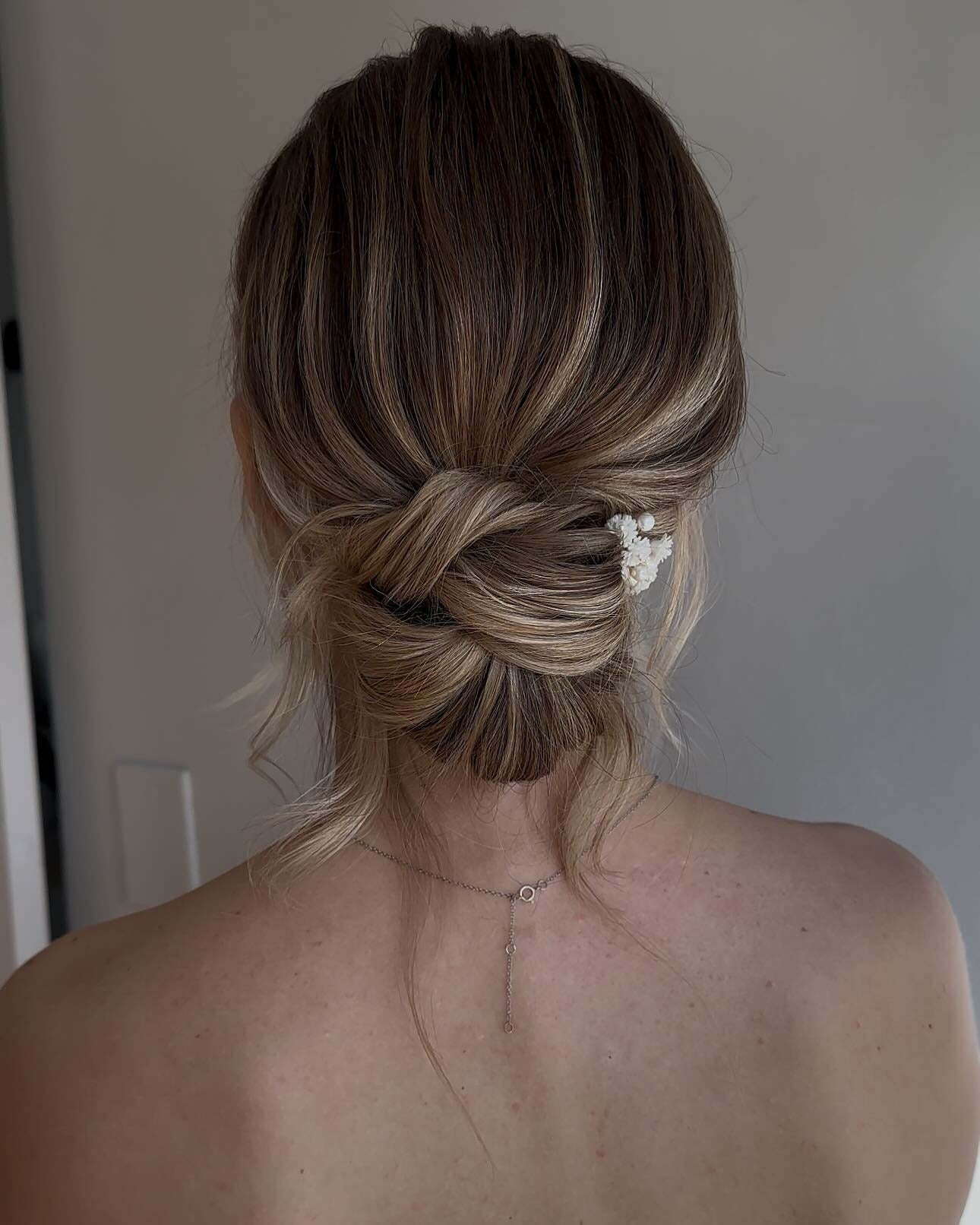 3. romantisches Brötchen mit weichen Highlights und floralen Akzent (niedriges, unordentliches Haarbrötchen)