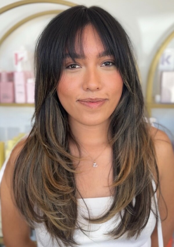 Weicher und dimensionaler, brünettfarbener, langgestufter Haarschnitt mit zartem Pony