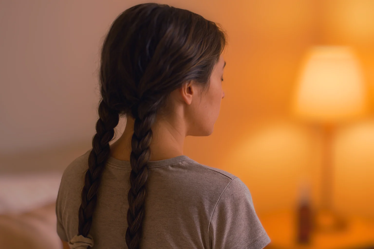 Eine Frau sitzt im Bett mit lockerem geflochtenem Haar, Satin-Kissenbezug und einer entspannten nächtlichen Haarroutine vor dem Schlafengehen.