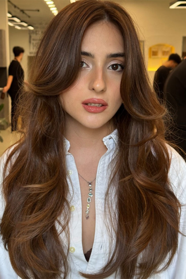 Fließendes langes kastanienbraunes Haar mit gefiederten Schichten, die das Gesicht umrahmen